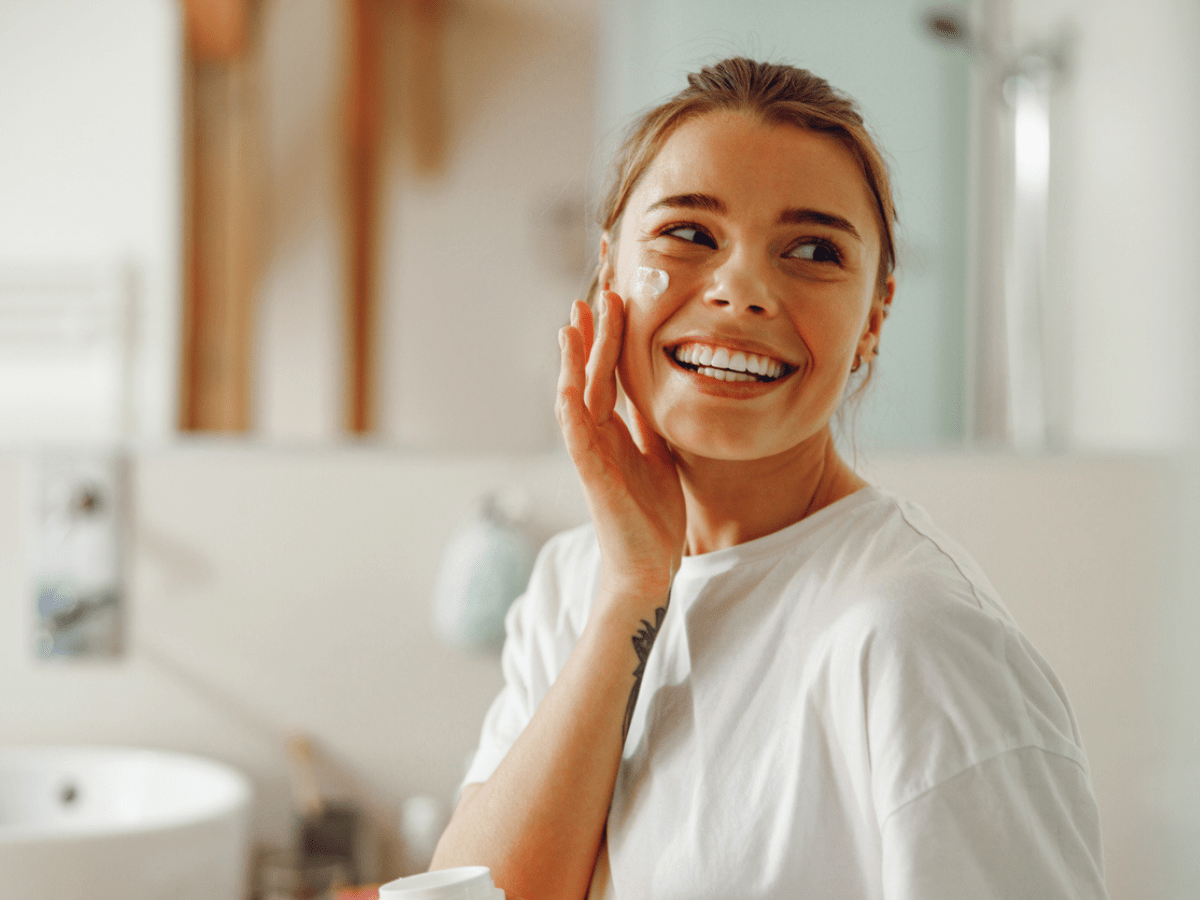 woman in bathroom smiling and touching her cheek